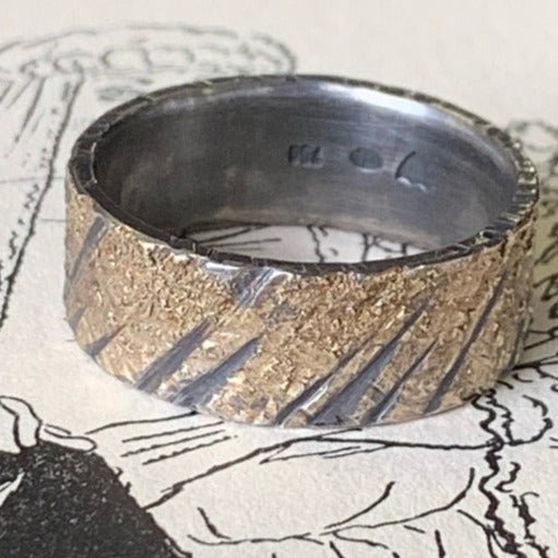 Gold Strike oxidised wedding ring by Jeanette Dyke. Handcrafted in oxidised sterling silver with 18ct rose gold, featuring a striking, textured design for a bold statement.
