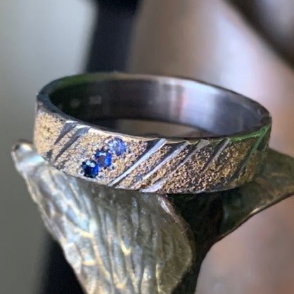 Gold Strike wedding ring by Jeanette Dyke. Handcrafted in 9ct white gold and 18ct yellow gold, featuring three blue sapphires for a striking, unique design.